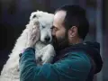 Un homme barbu enlace tendrement un chien blanc aux yeux fermés. Un moment de pur candilat chien.